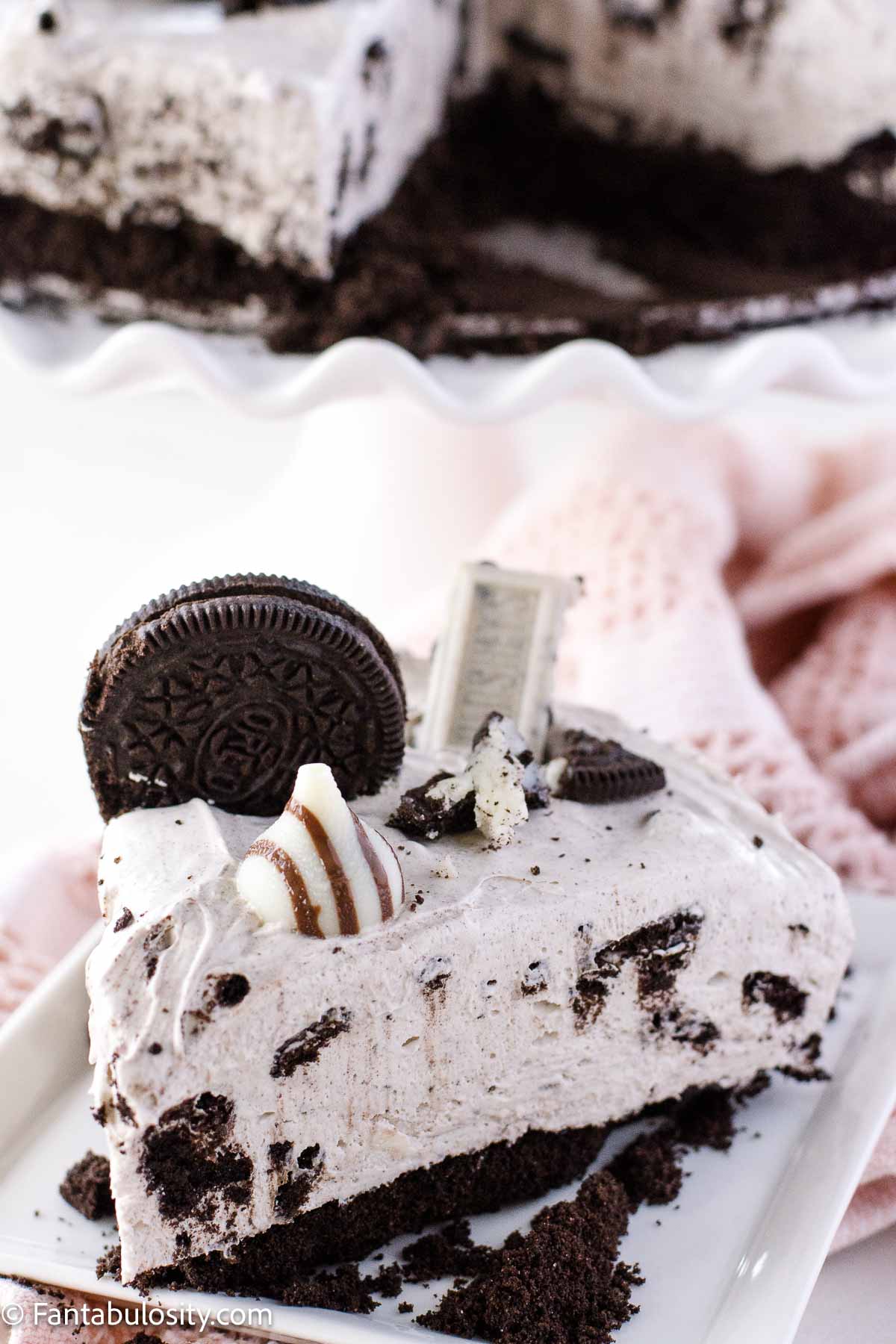 Slice of Oreo cheesecake on a plate, sitting in front of whole cheesecake.