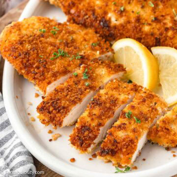 Crispy panko chicken breasts sliced on plate, with lemon wedges sitting beside them.