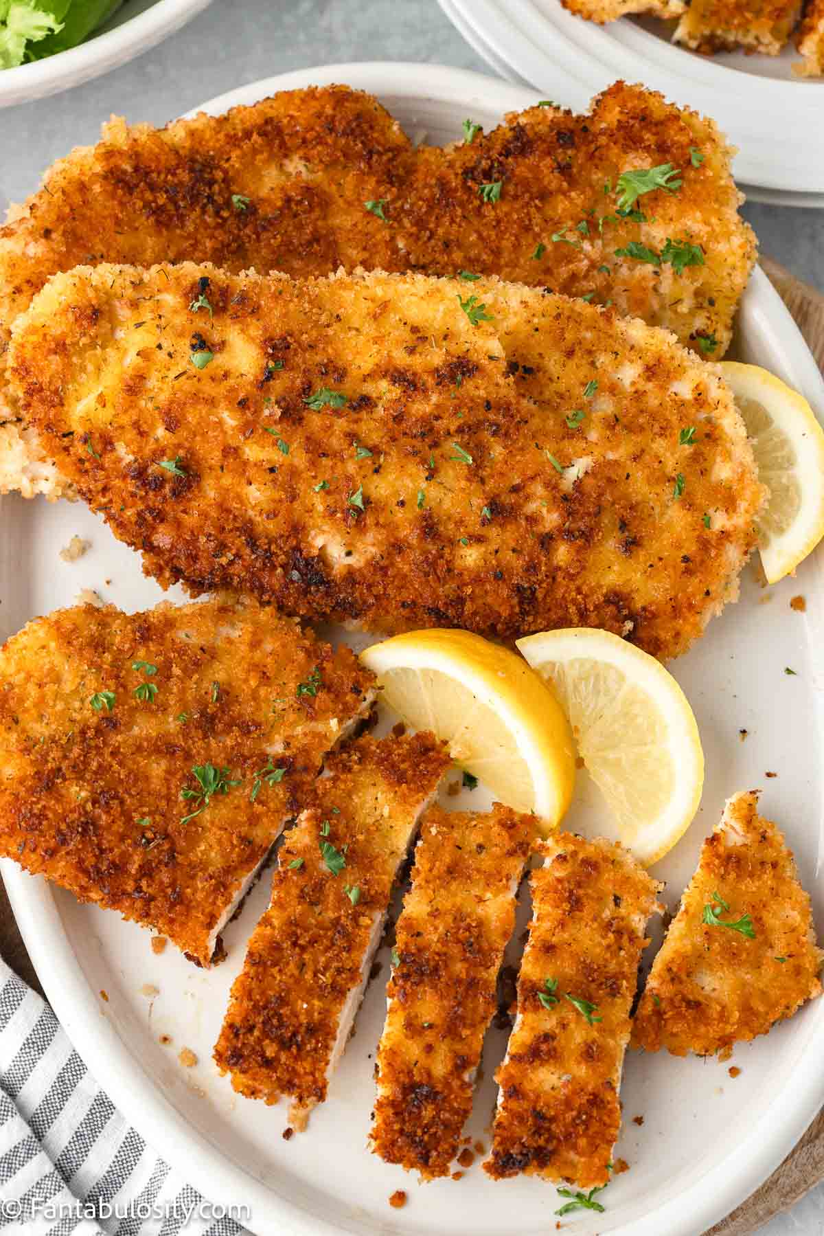 Panko chicken sliced and whole, on round plate with lemons.