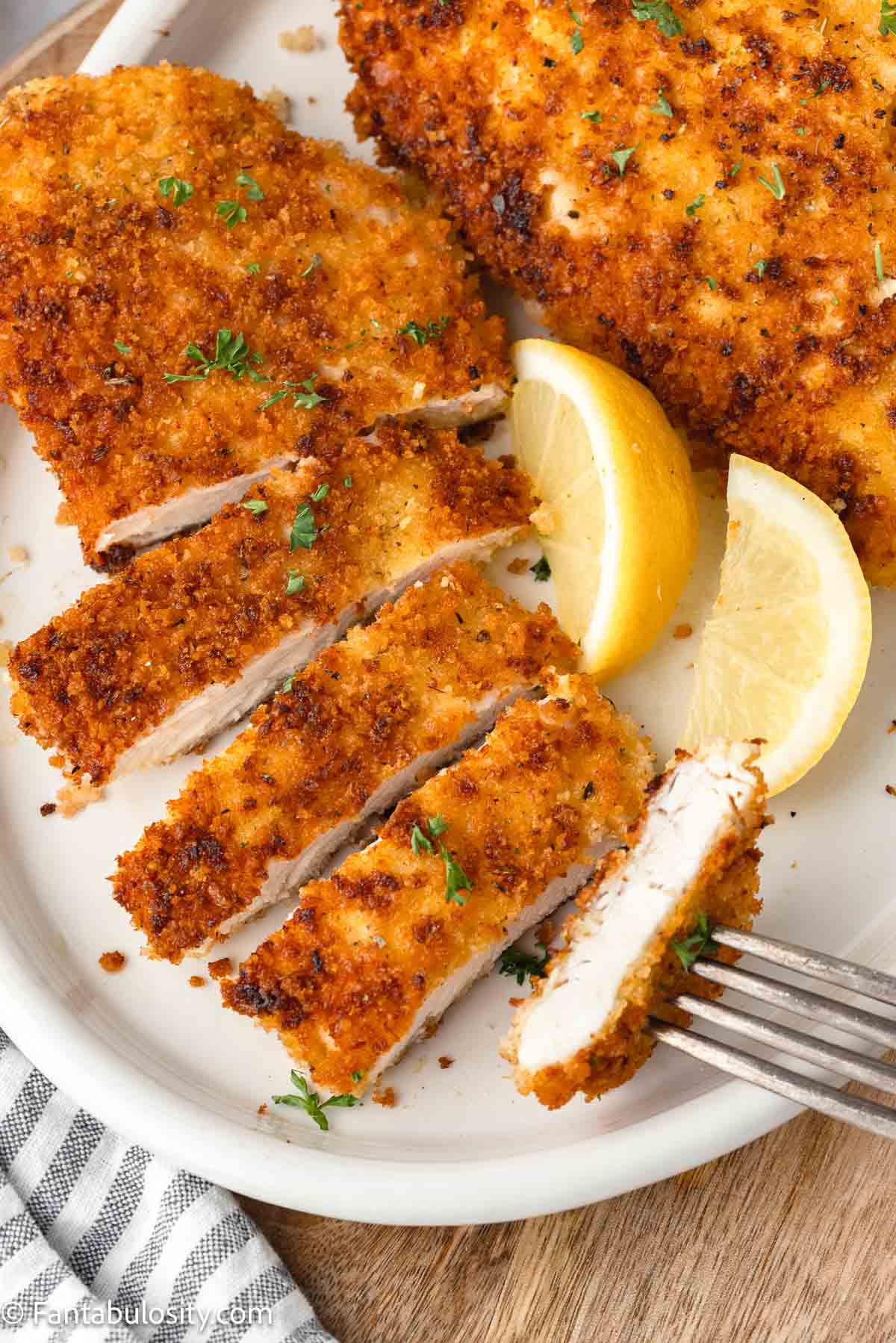 Panko chicken breasts sliced on plate, with lemon slices.
