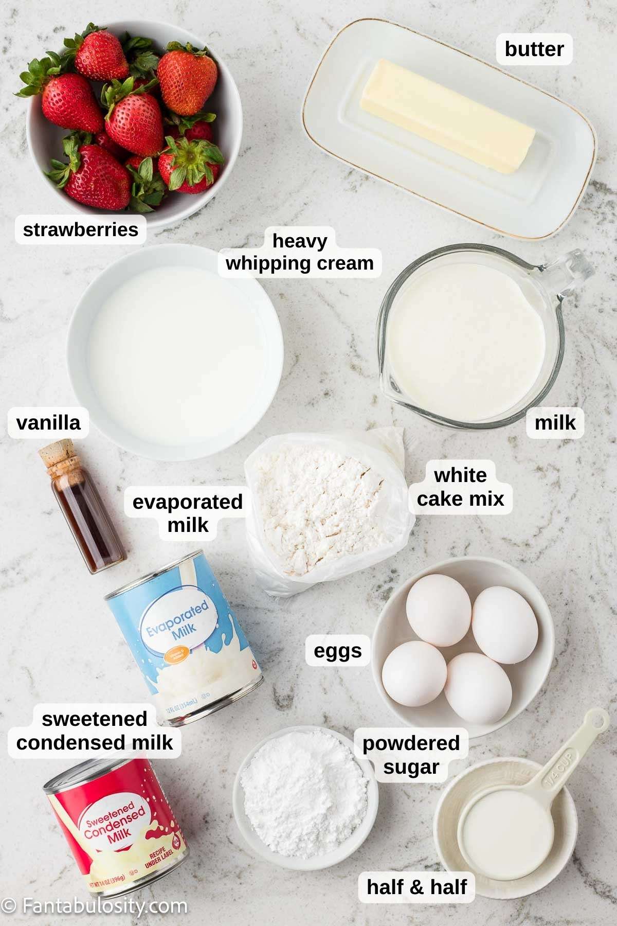 Ingredients to make Strawberry Whipped Cream Cake sitting on marble background.