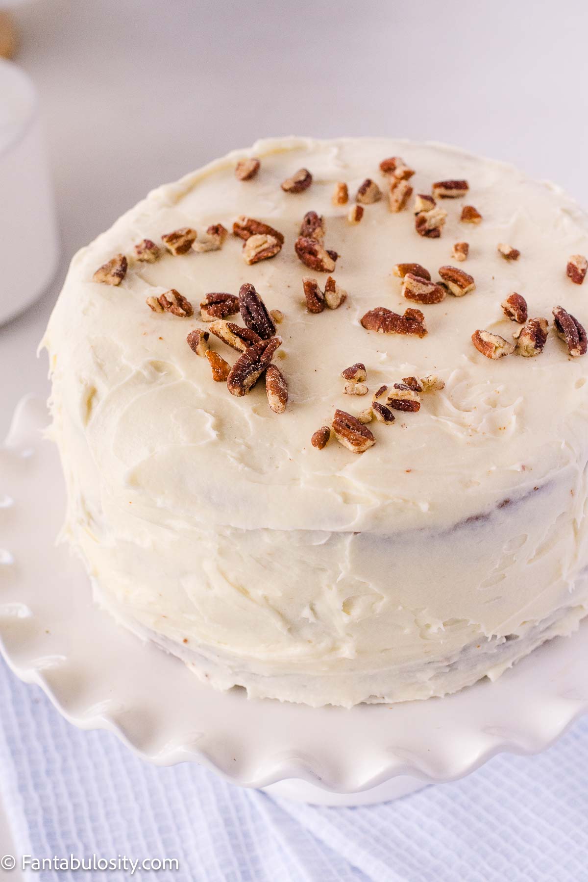 Whole carrot cake on white cake stand.