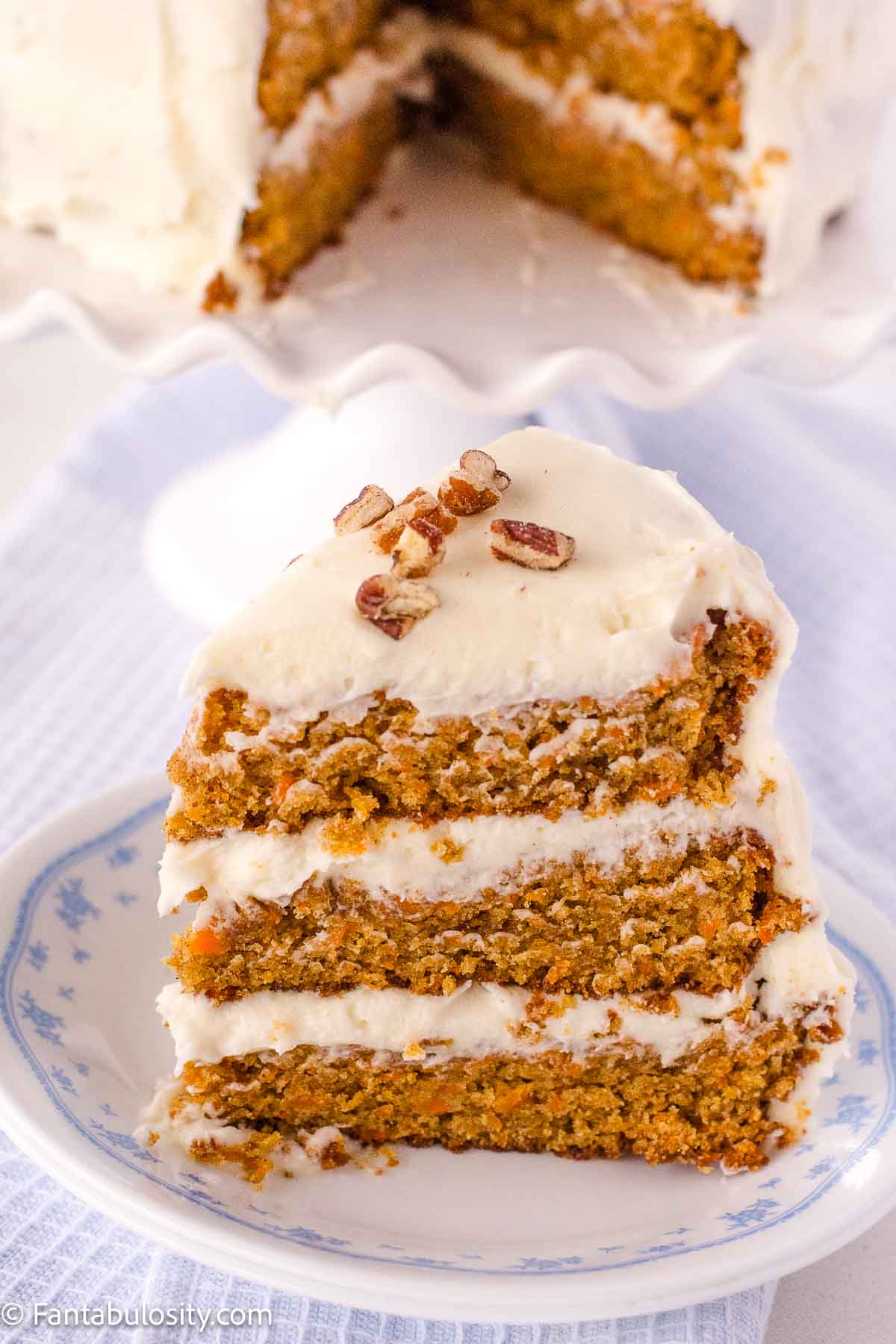 A slice of carrot cake with cream cheese icing on vintage plate.