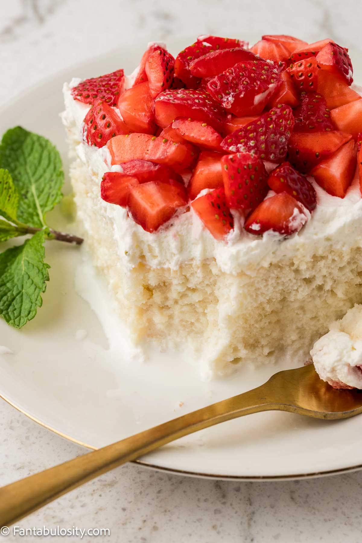 Slice of Strawberry Whipped Cream Cake on round plate, with fork taking a bite out of the corner.