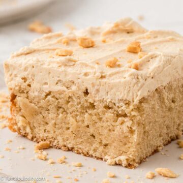 Slice of peanut butter cake with peanut butter frosting on top, sitting on a plate.