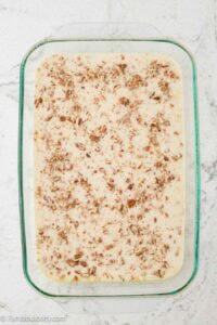 Banana and milk mixture in baking pan with pecans sprinkled on top.