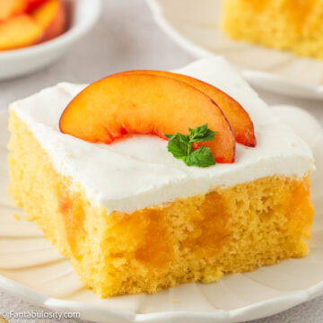 Slice of peaches and cream cake on plate with fresh peaches on top.