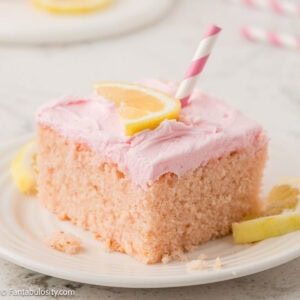 Slice of pink lemonade cake, with pink and white striped straw sticking out the top.