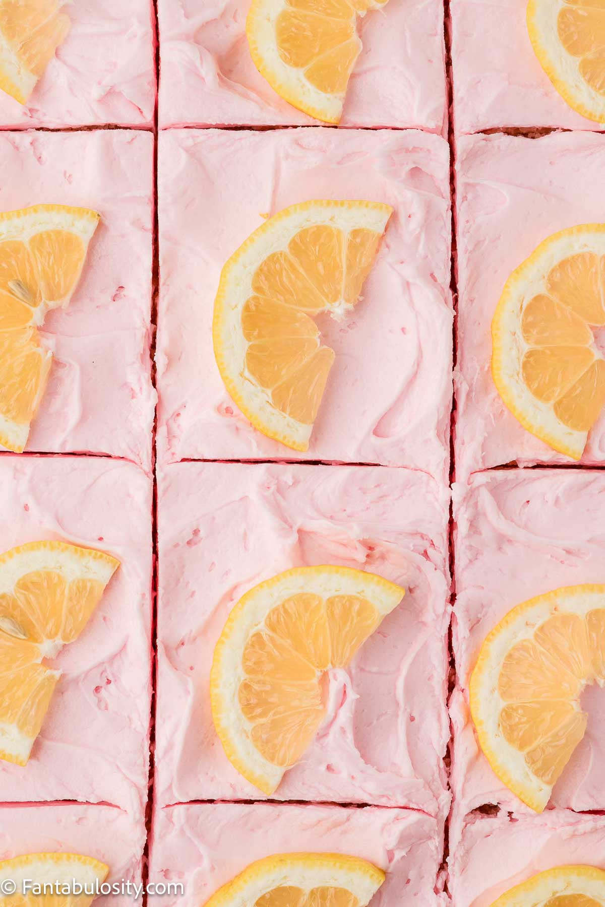 Pink lemonade cake, sliced in baking pan, with lemon wedges on top.
