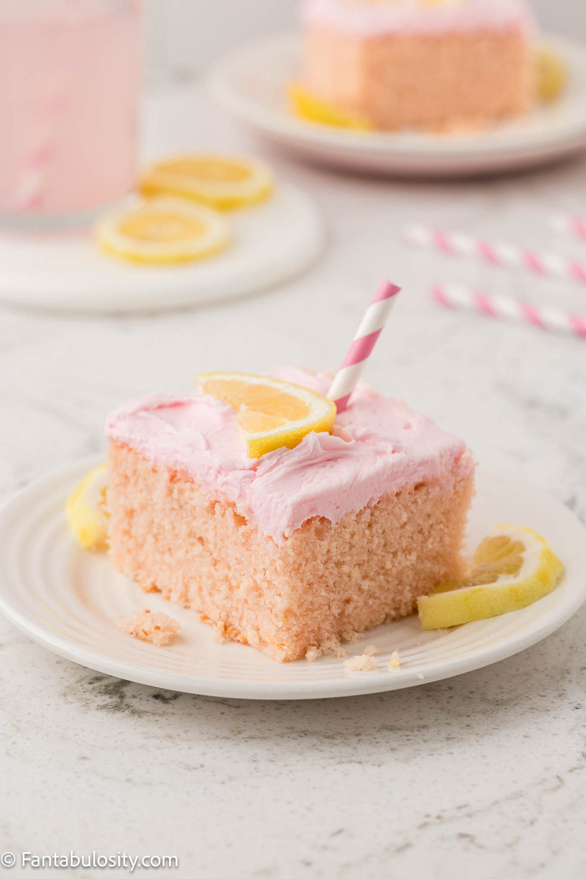Slice of pink lemonade cake with a straw sticking out of the top, and sitting on a round plate.