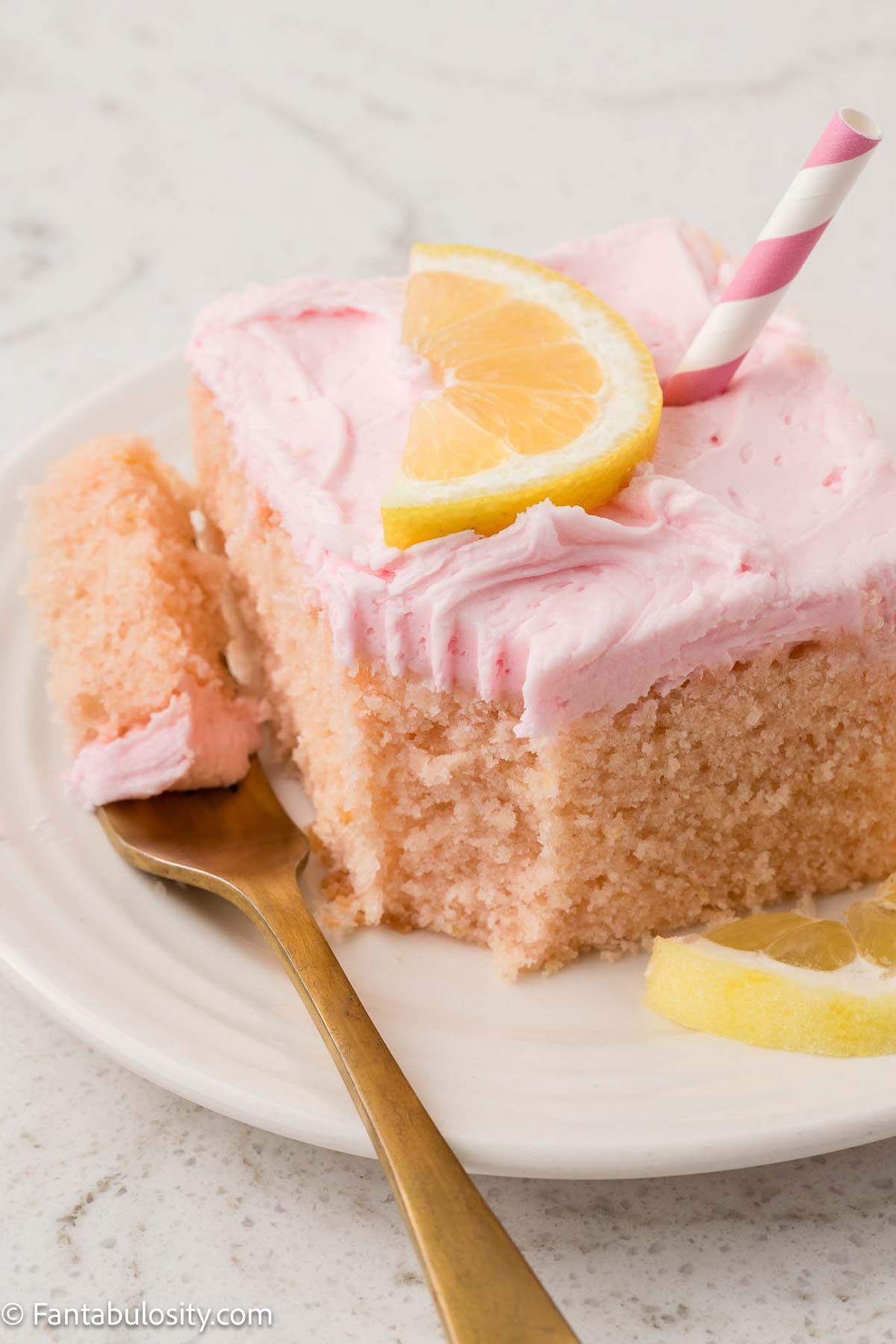 Slice of pink lemonade sheet cake on plate, with a fork taking a bite off of the corner.