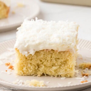 Slice of coconut sheet cake on a plate, next to other plate with cake.