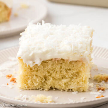 Slice of coconut sheet cake on a plate, next to other plate with cake.