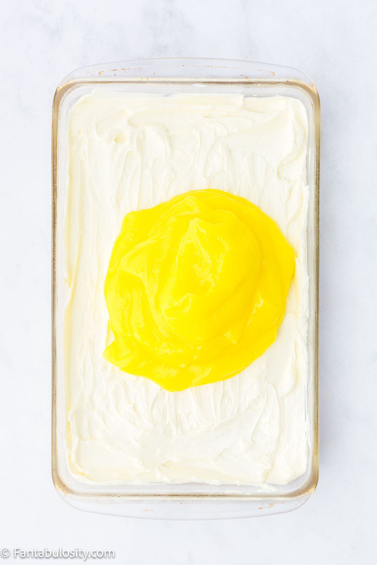 Lemon pie filling on top of cream cheese mixture in baking pan.