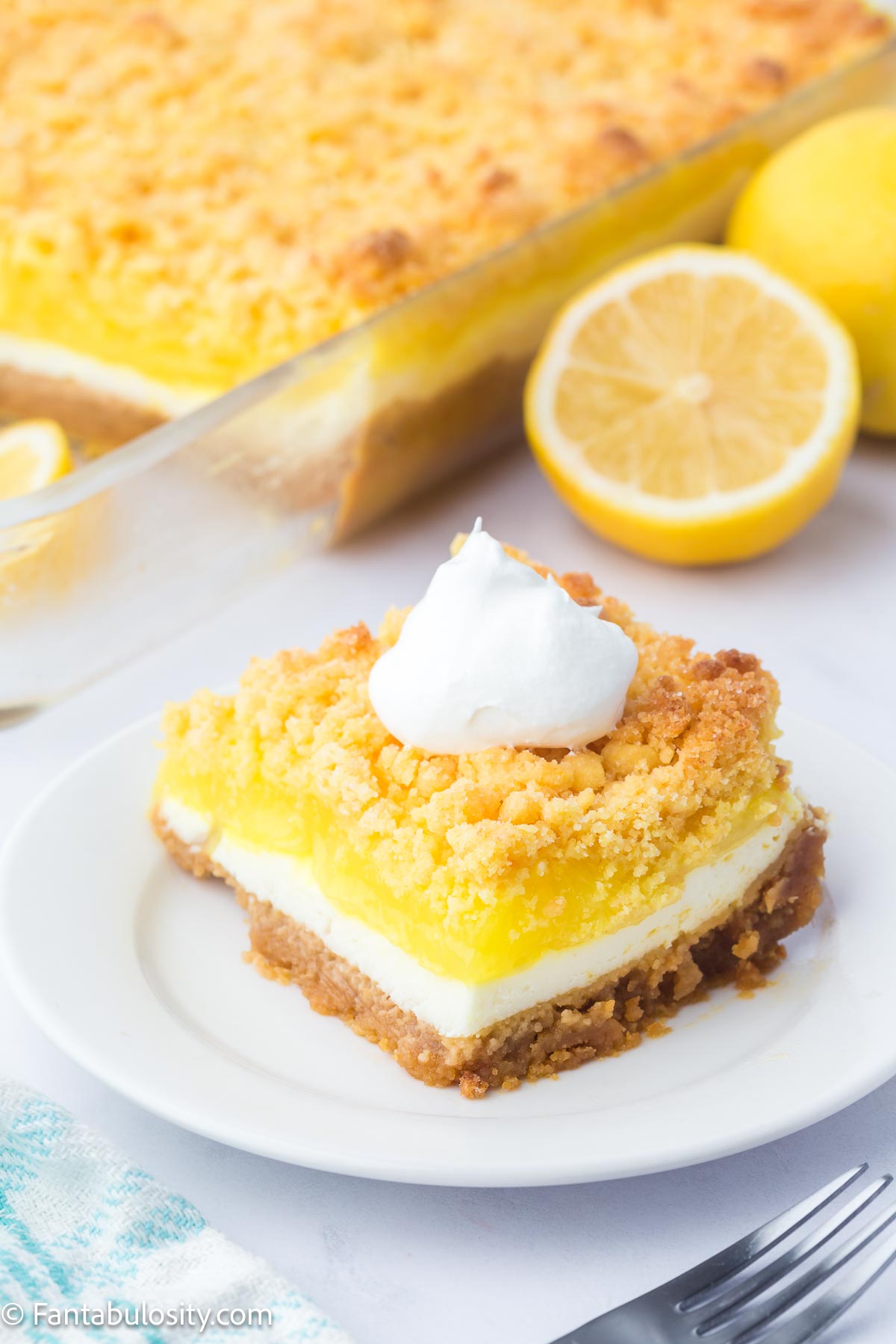 Slice of lemon dump cake topped with whipped cream, sitting on round plate.