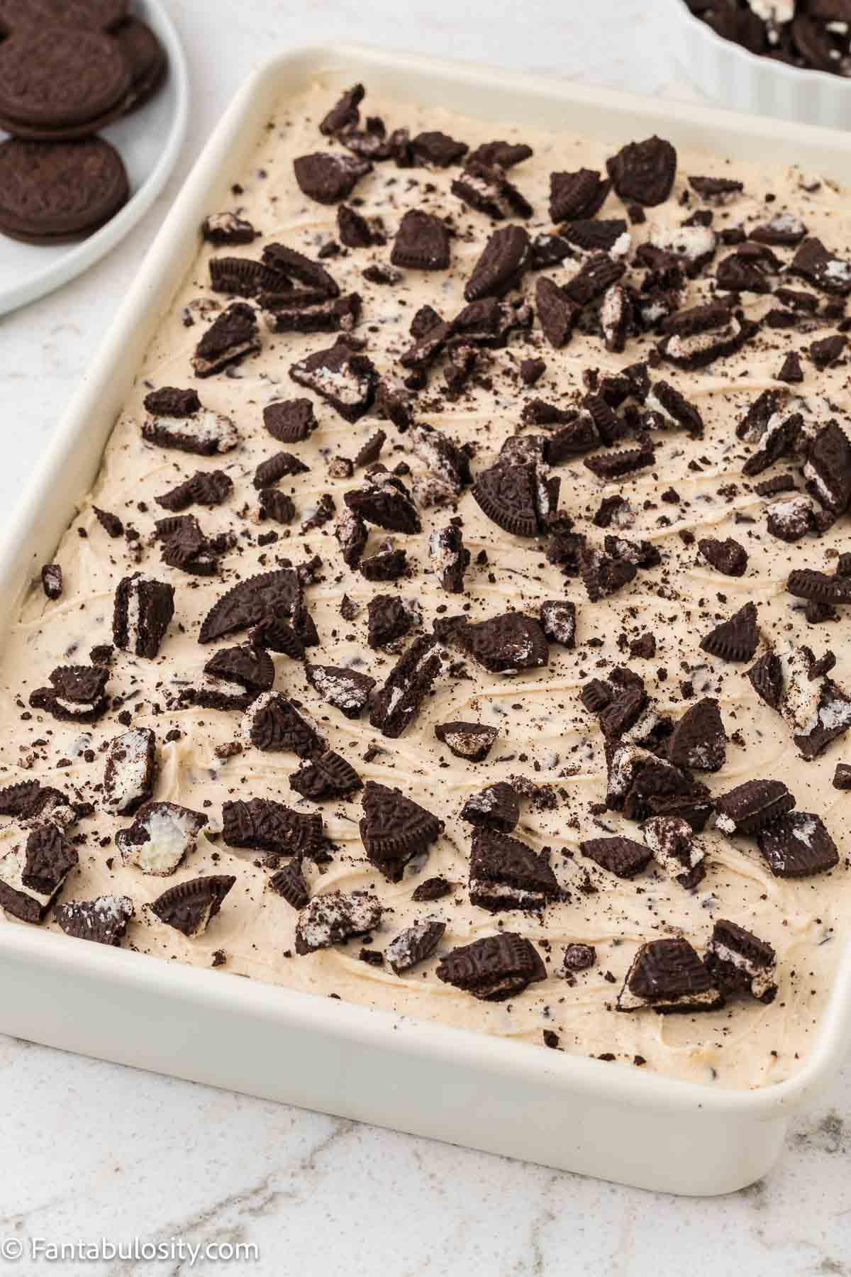 A 9x13 baking dish, that has a chocolate sheet cake in it with a cookie dough frosting and crushed Oreos on top.