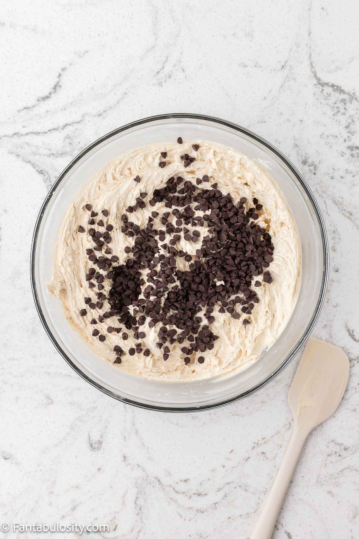 Chocolate chips added to mixing bowl with cookie dough frosting ingredients.