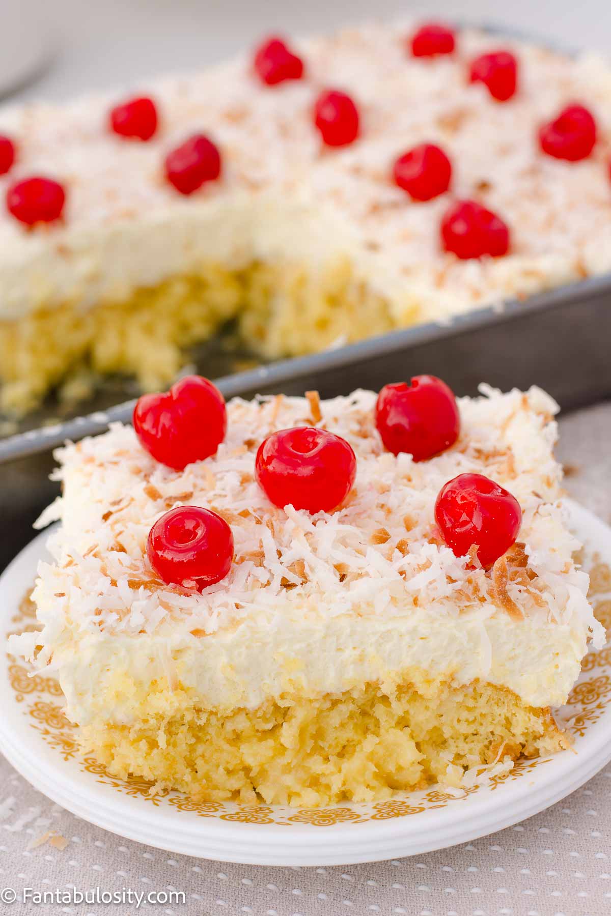 A slice of pina colada cake on a vintage plate, next to a pan of cake.