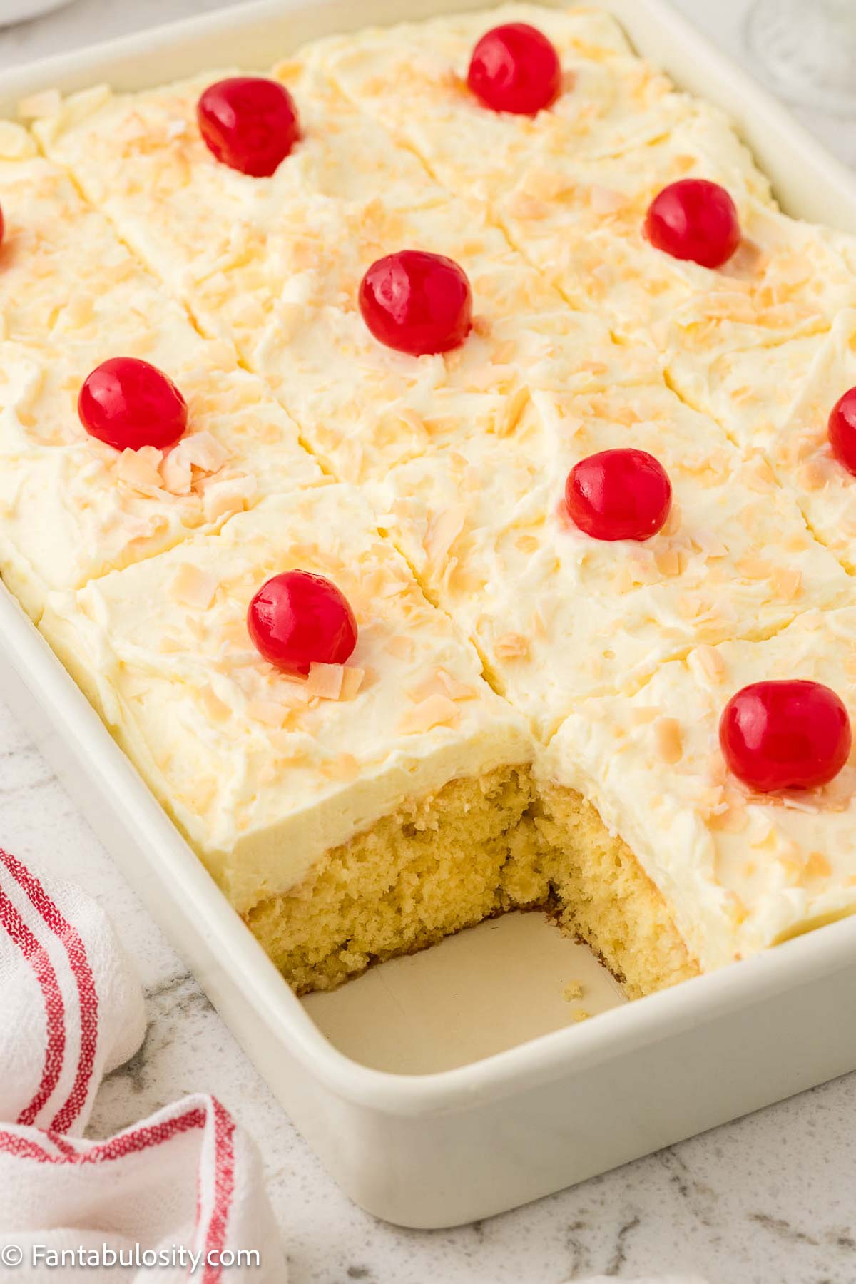 Pina colada sheet cake in baking pan, topped with coconut and cherries.