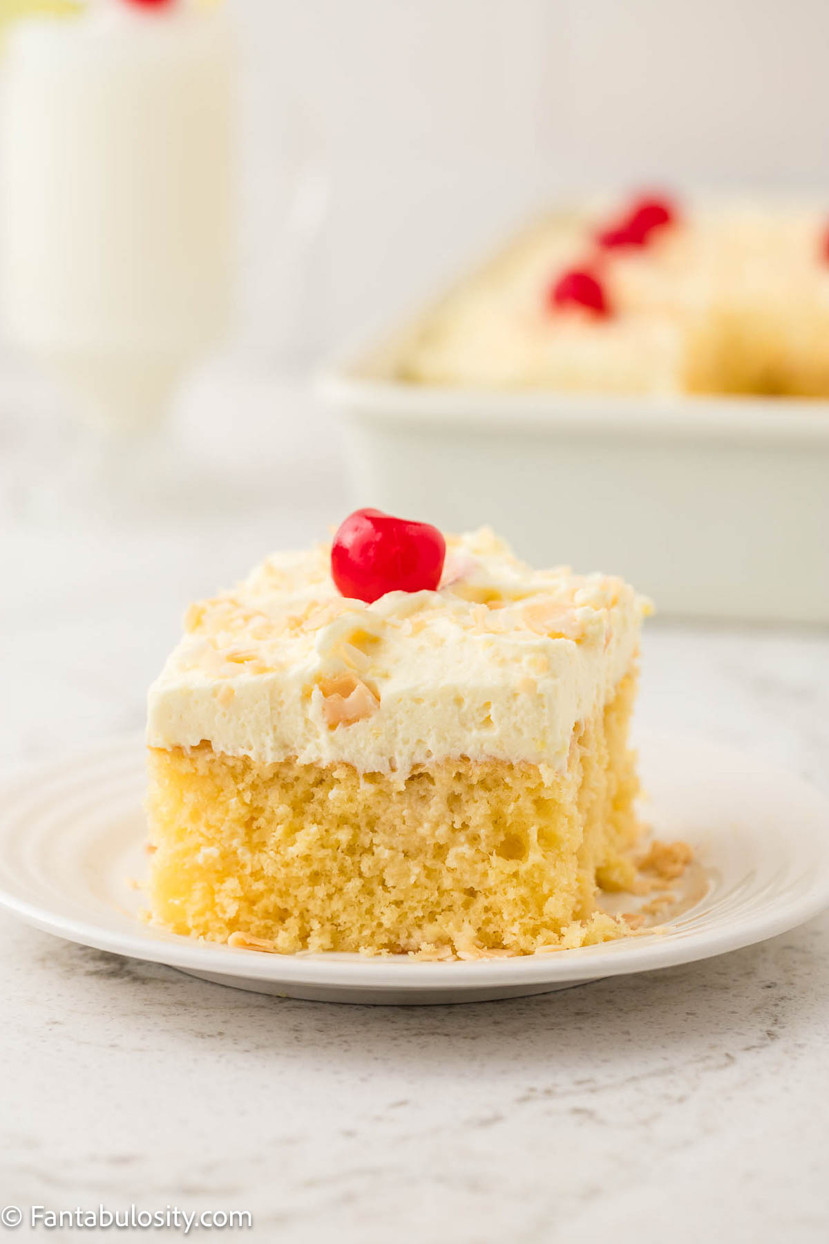 Slice of pina colada cake, topped with a cherry and coconut, sitting on a round plate.