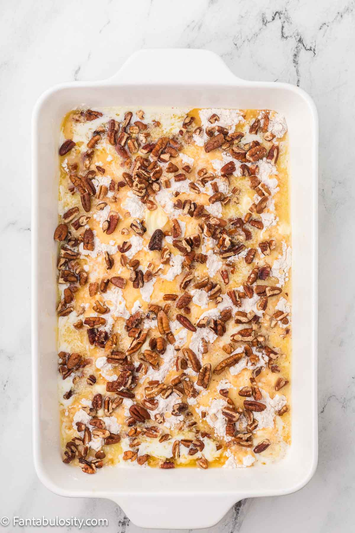 Cake mix poured on top of pumpkin mixture, and nuts poured on top of cake mix.
