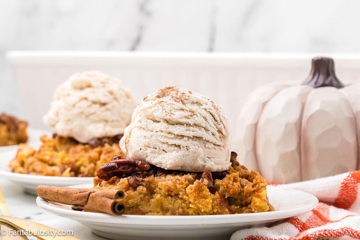 Serving of pumpkin dump cake on plate with vanilla ice cream on top.