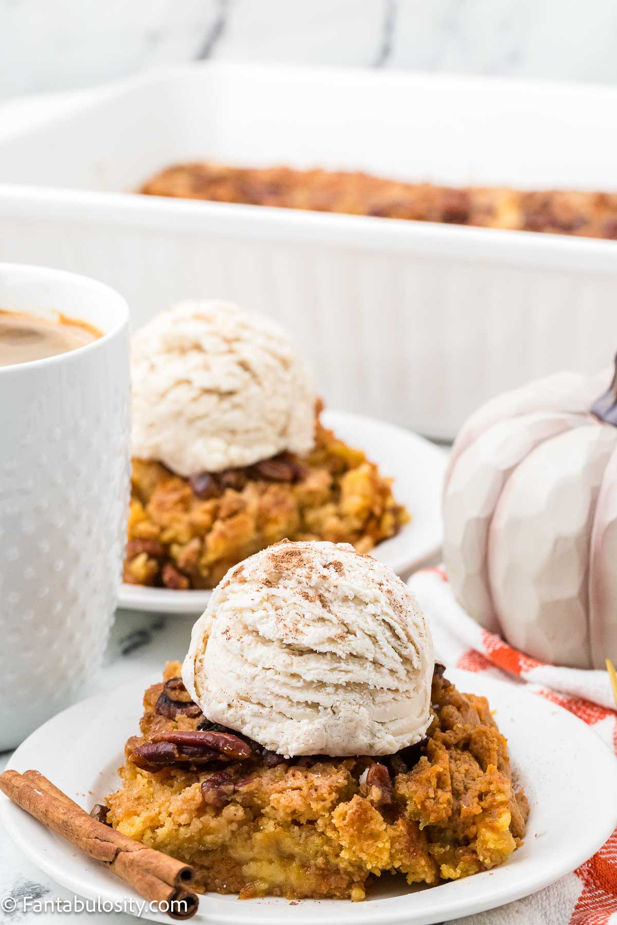 Serving of pumpkin dump cake on round plate, topped with vanilla ice cream.