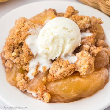 A serving of snickerdoodle apple dump cake in a round plate, topped with vanilla ice cream.