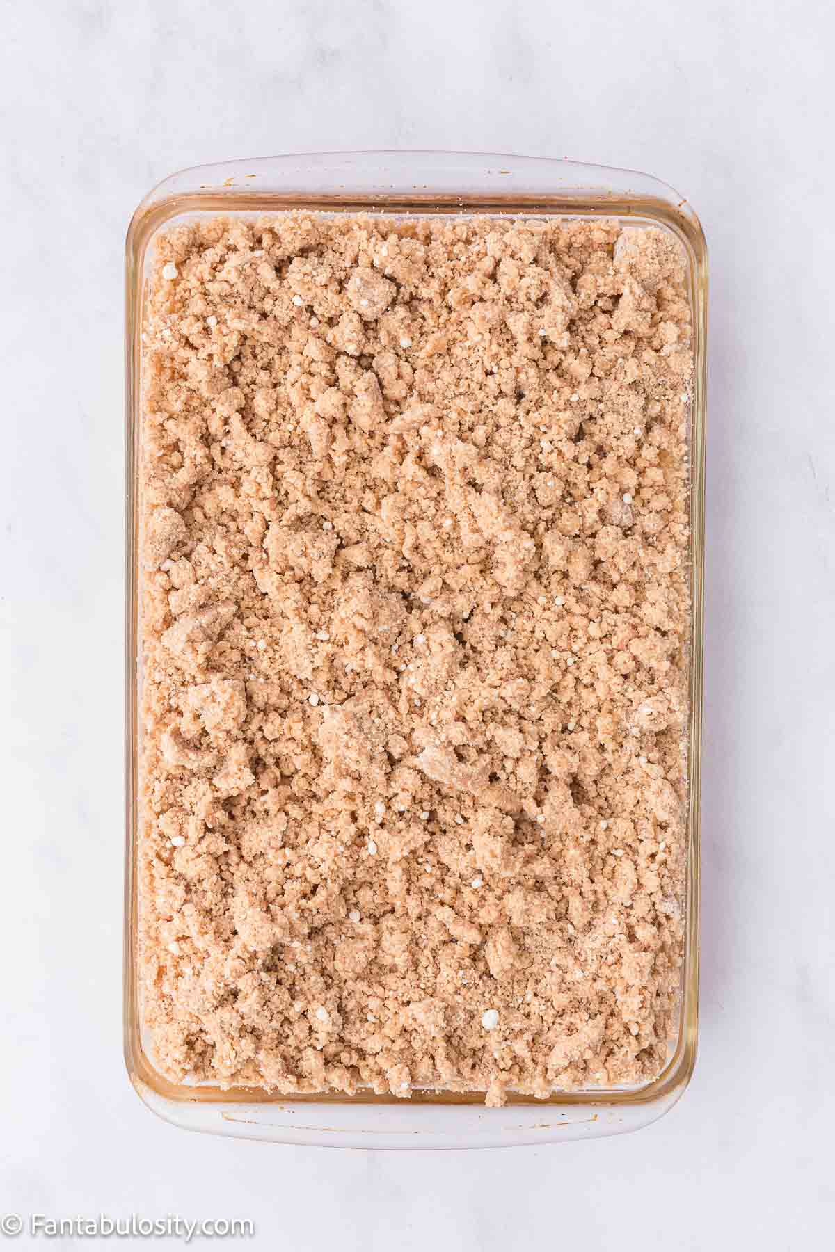 Cookie mix with butter, sprinkled on top of apple pie filling in baking dish.
