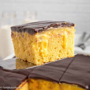 A slice of Boston Cream Pie Poke Cake on a spatula, resting above baking pan.