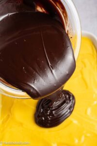 Chocolate ganache being poured over the Boston Cream Pie poke cake.