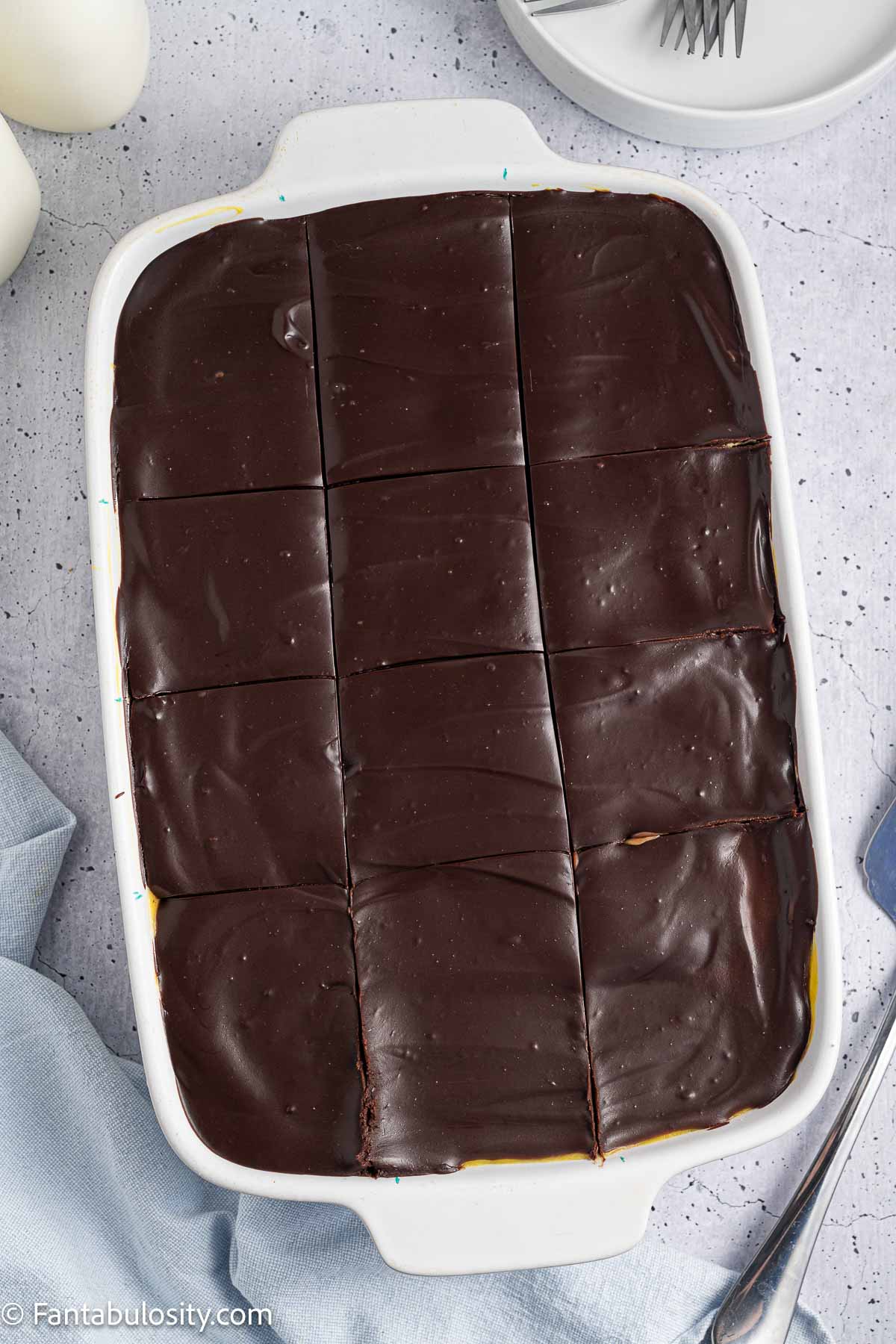 Chocolate ganache spread on top of cake and sliced in to slices, in baking pan.