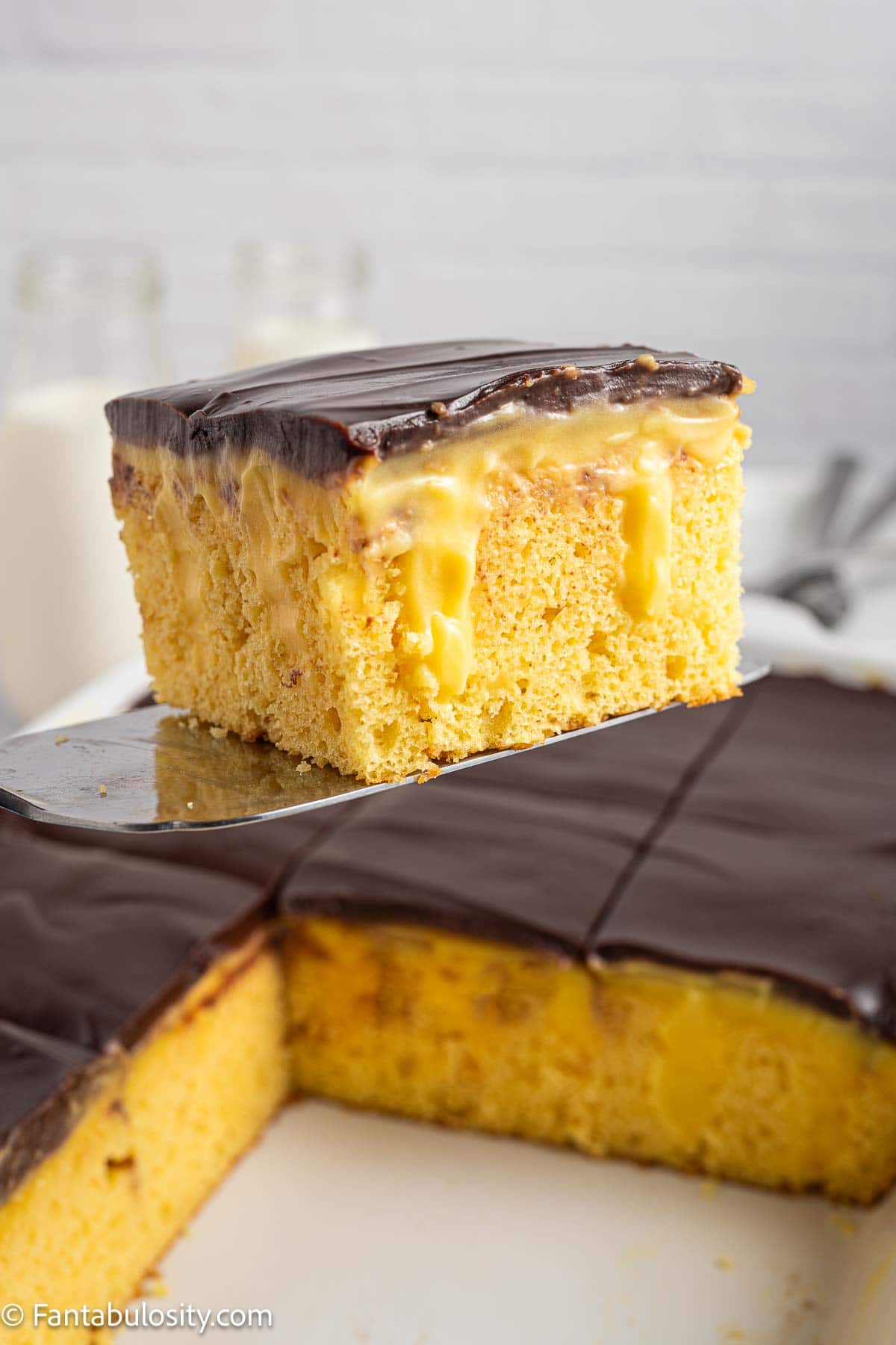 A slice of Boston Cream Pie Poke Cake on a spatula, resting above a baking pan. 
