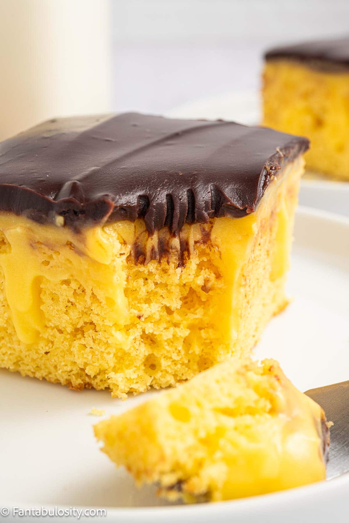 Slice of Boston Cream Pie Poke Cake on a plate with fork taking a bite out of it. 