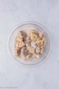 Small pieces of cinnamon rolls sitting in sugar cinnamon mixture in mixing bowl.