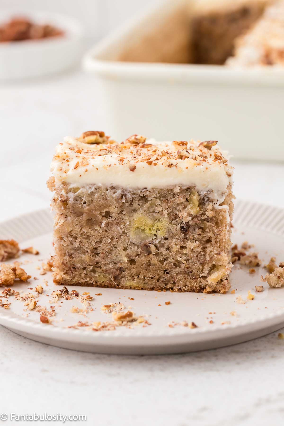 Slice of hummingbird cake on plate, frosted with cream cheese frosting.