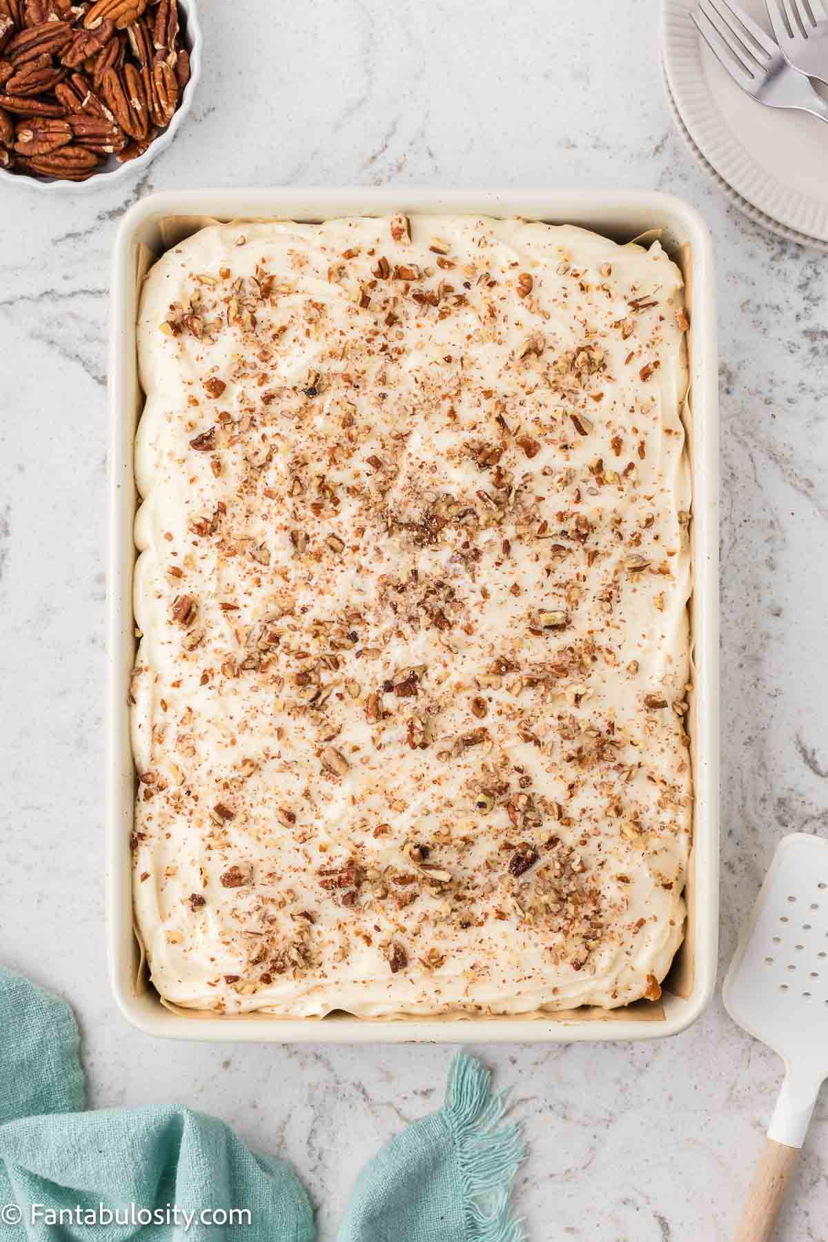 Baked hummingbird cake in baking dish, frosted with pecans.