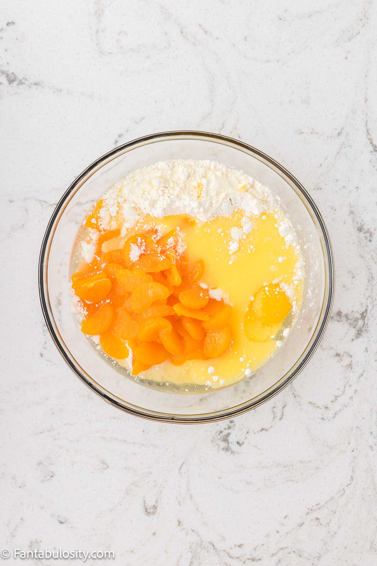 Cake mix, eggs, oranges, all added in a mixing bowl.