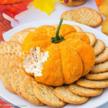 Pumpkin cheese ball on plate surrounded by crackers.