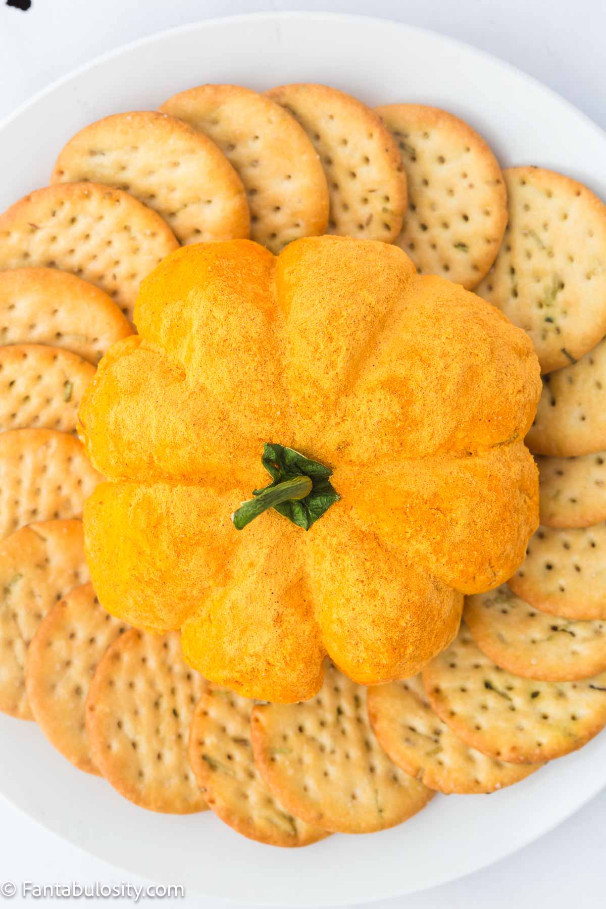 Finished pumpkin cheese ball sitting on plate, surrounded by crackers.