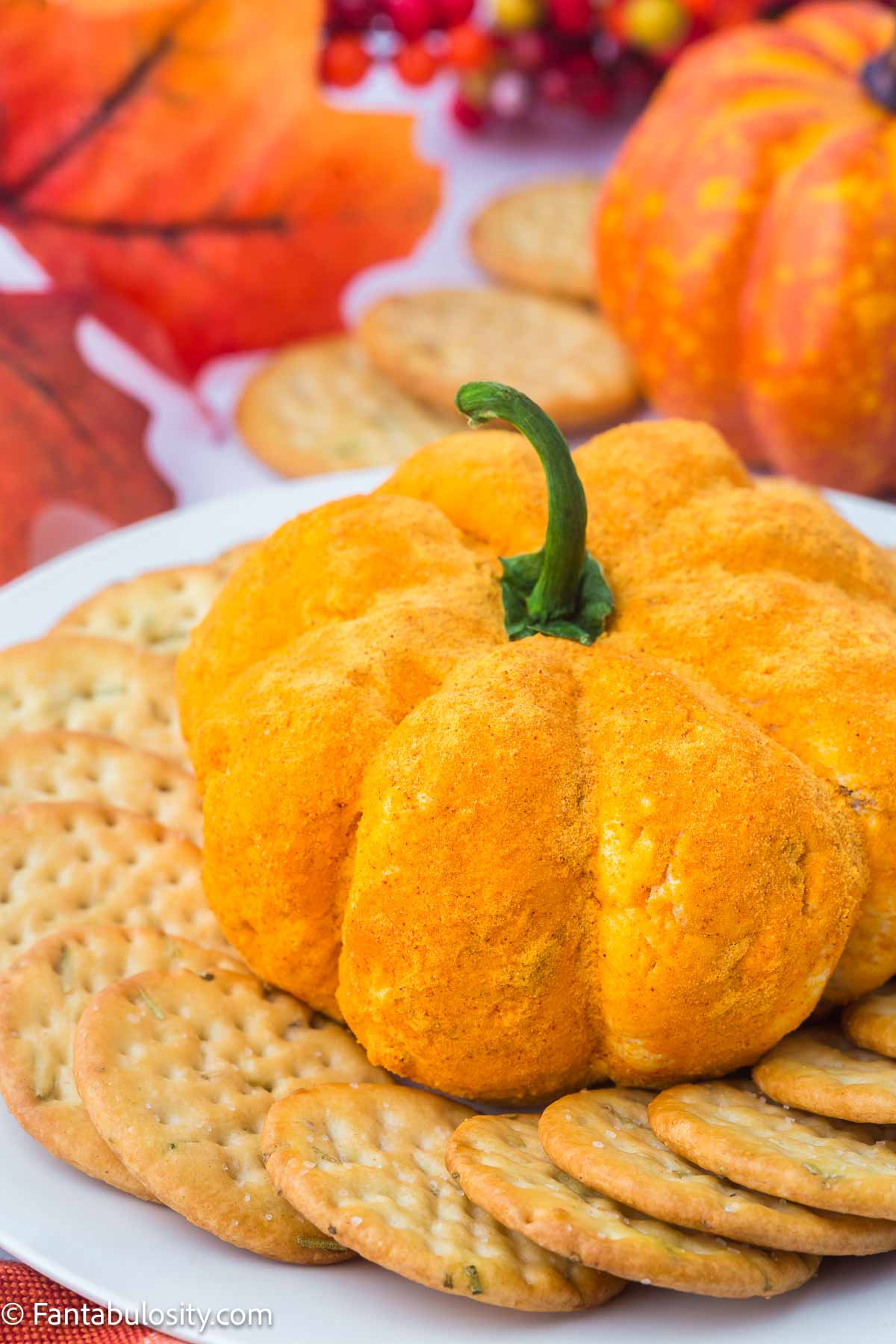 Pumpkin cheese ball sitting on plate, with round crackers.