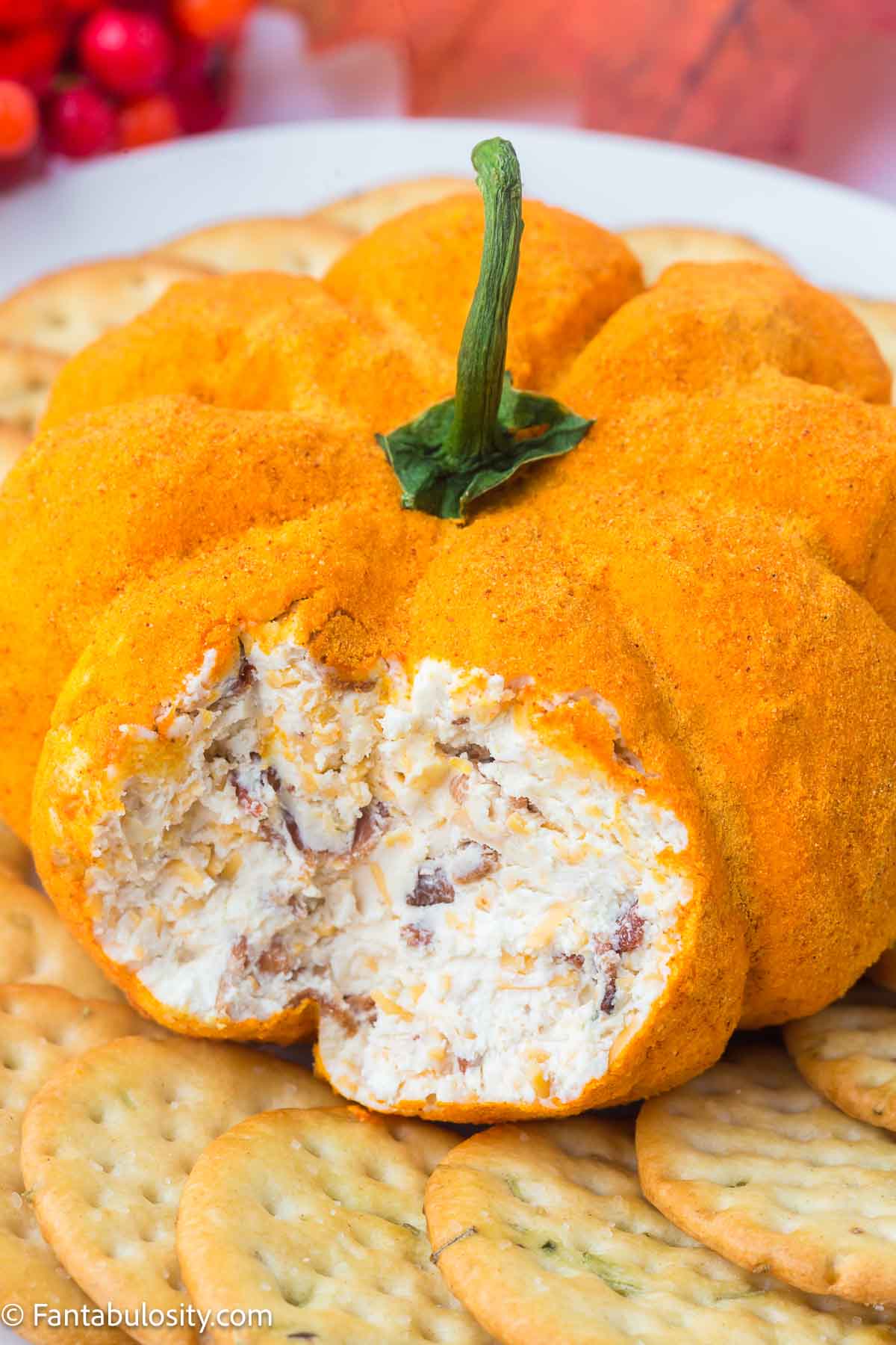 Pumpkin cheese ball on a plate, surrounded by crackers, and a bite taken out to show the inside of the cheese ball.