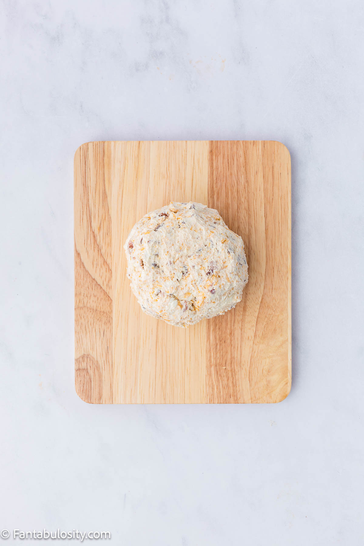 Cheese ball shaped in to a ball, sitting on a wooden cutting board.