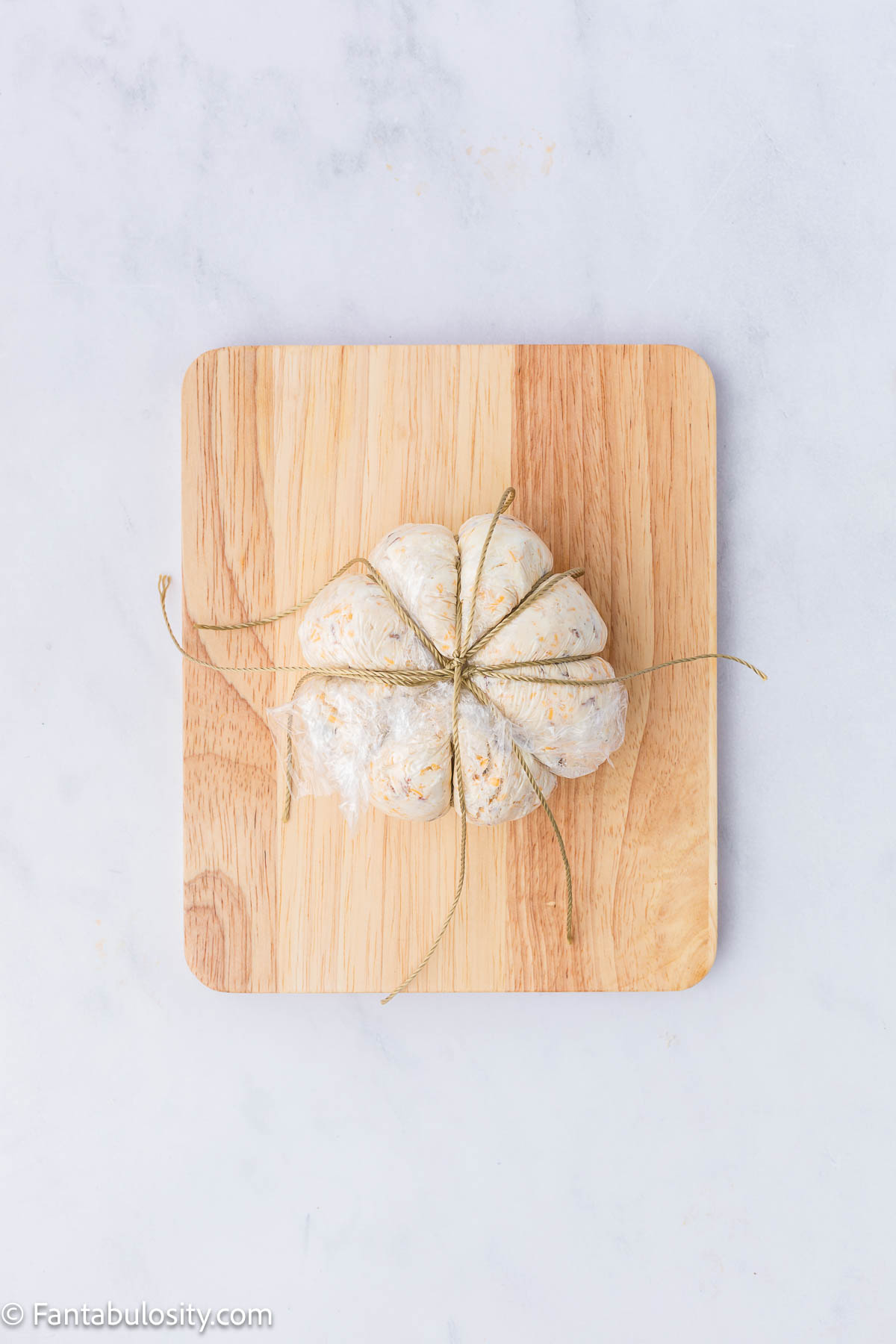 Cheese ball wrapped in plastic wrap and baking twine to create ridges.