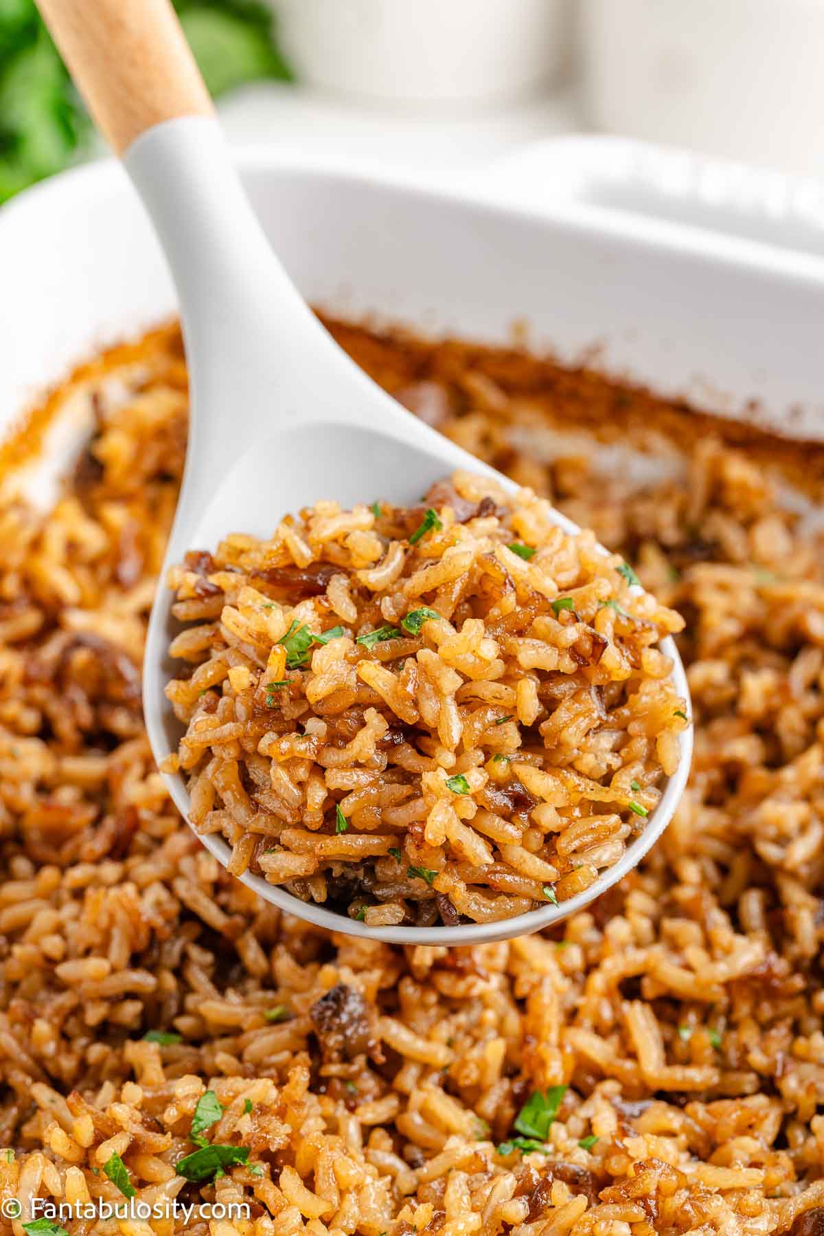 Stick of butter rice in a serving spoon, resting in the baking dish.