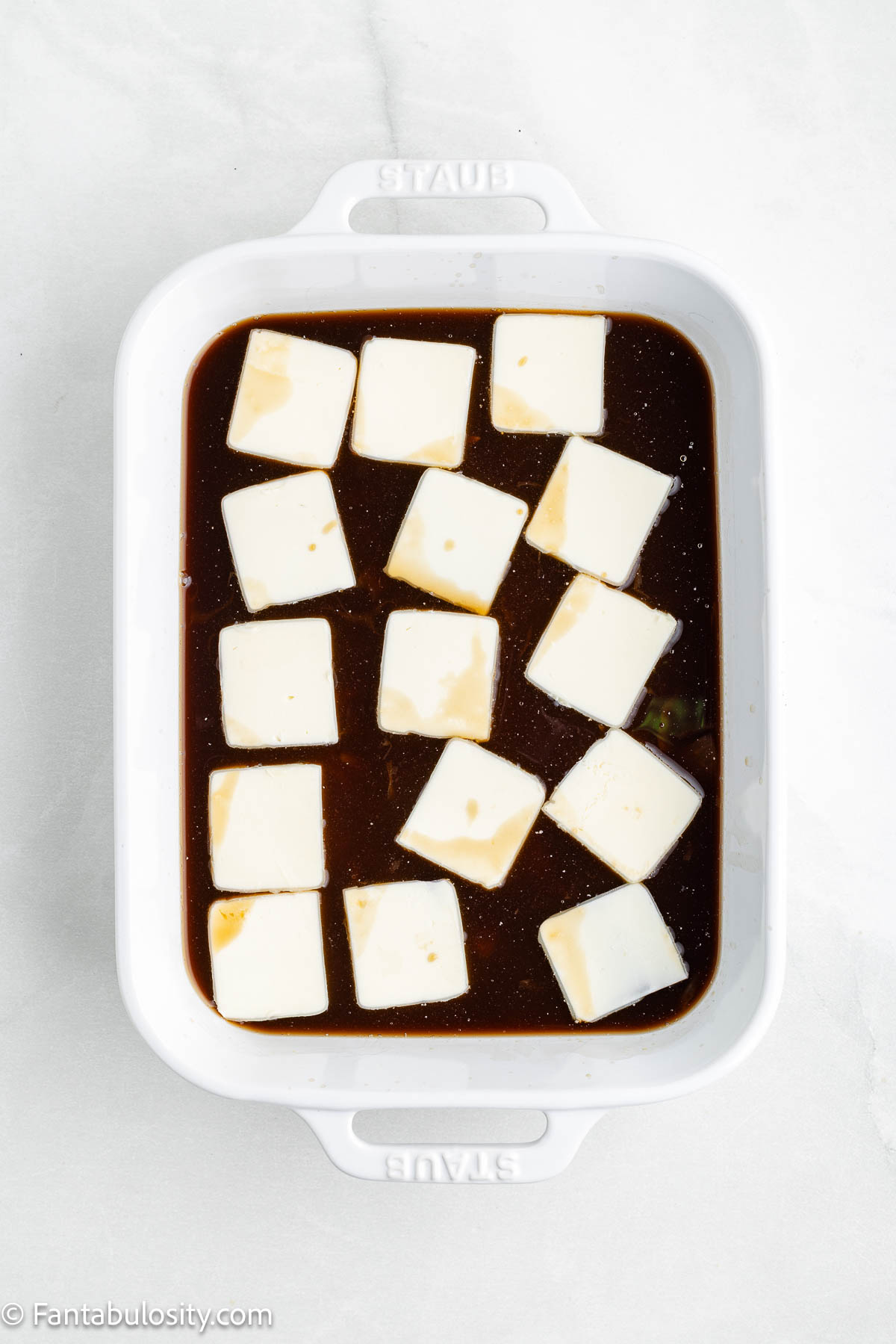 Sliced stick of butter sitting on top of rice and canned soup and broth.