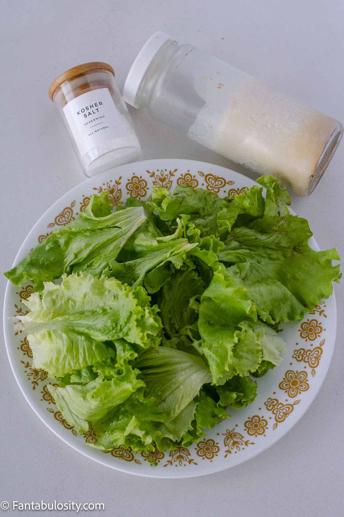Plate with leaf lettuce on it, sitting next to salt, and cold bacon grease in a jar.