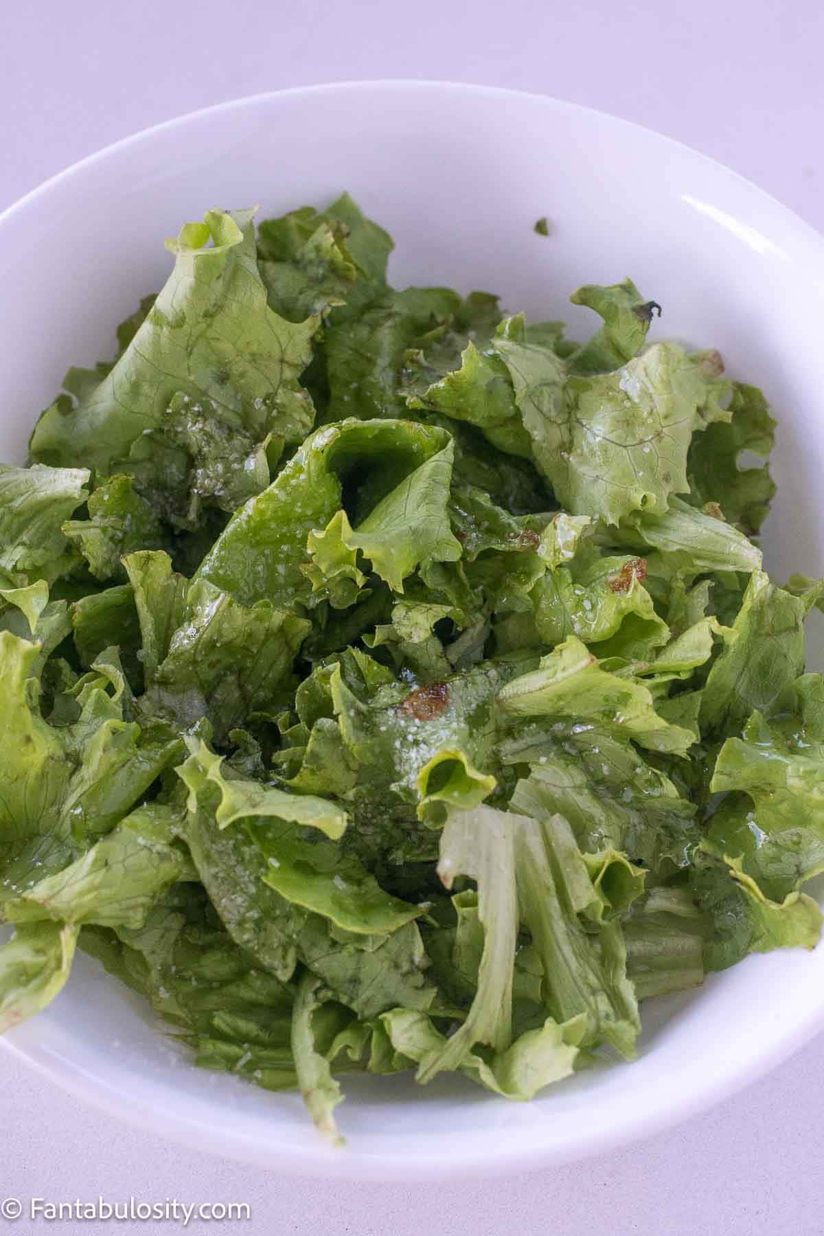Leaf lettuce in bowl that's topped with hot bacon grease and kosher salt.