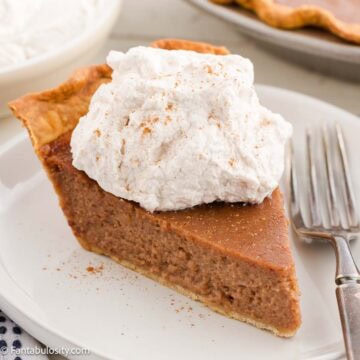A slice of apple butter pie topped with cinnamon whipped cream, sitting on a round plate.