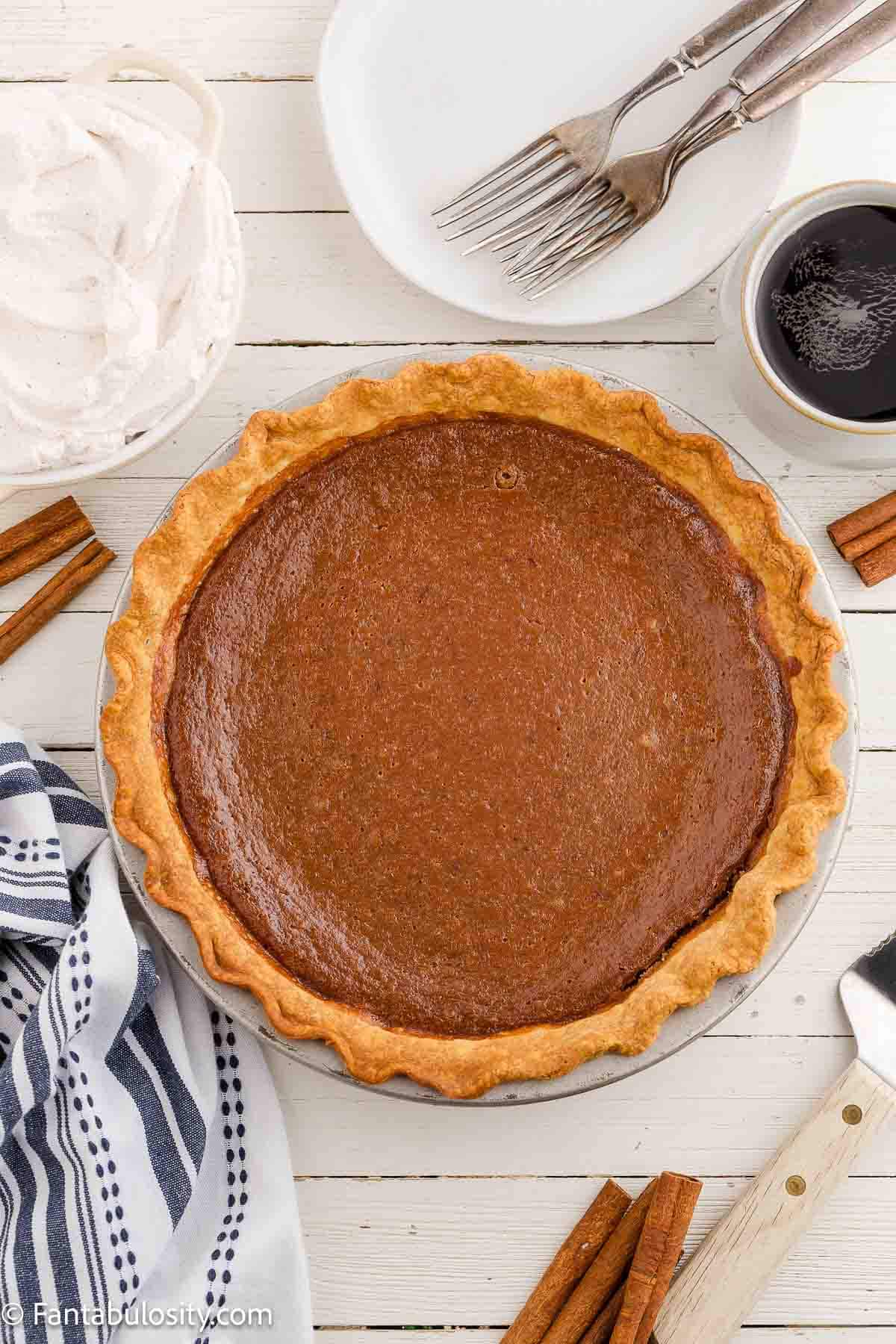 Baked apple butter pie, in pie dish, surrounded by plates and forks.